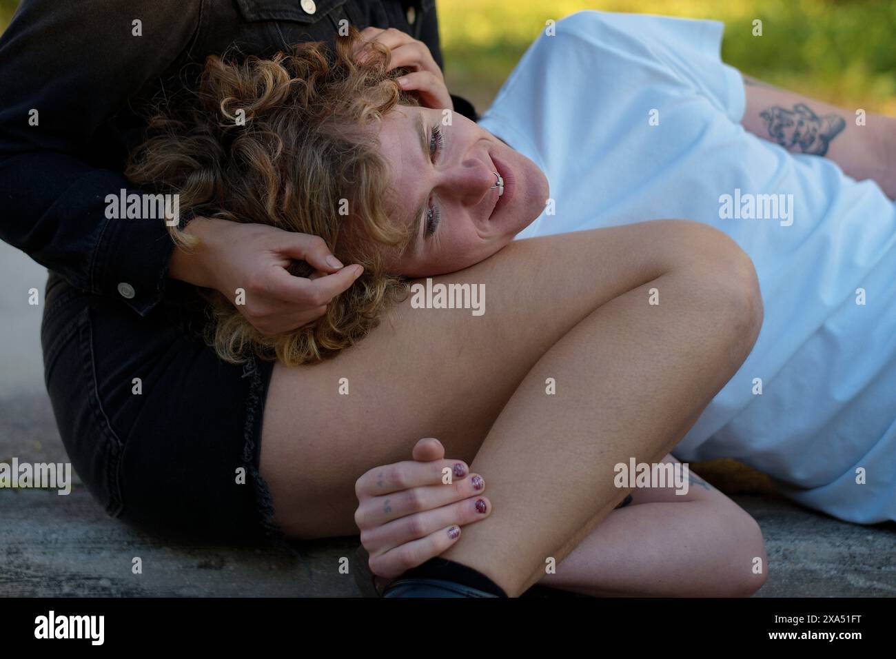 Donna sorridente sdraiata in grembo di qualcuno all'aperto, godendosi un momento informale e affettuoso. Foto Stock Donna sorridente sdraiata in grembo di qualcuno all'aperto, godendosi un momento informale e affettuoso. Foto Stock