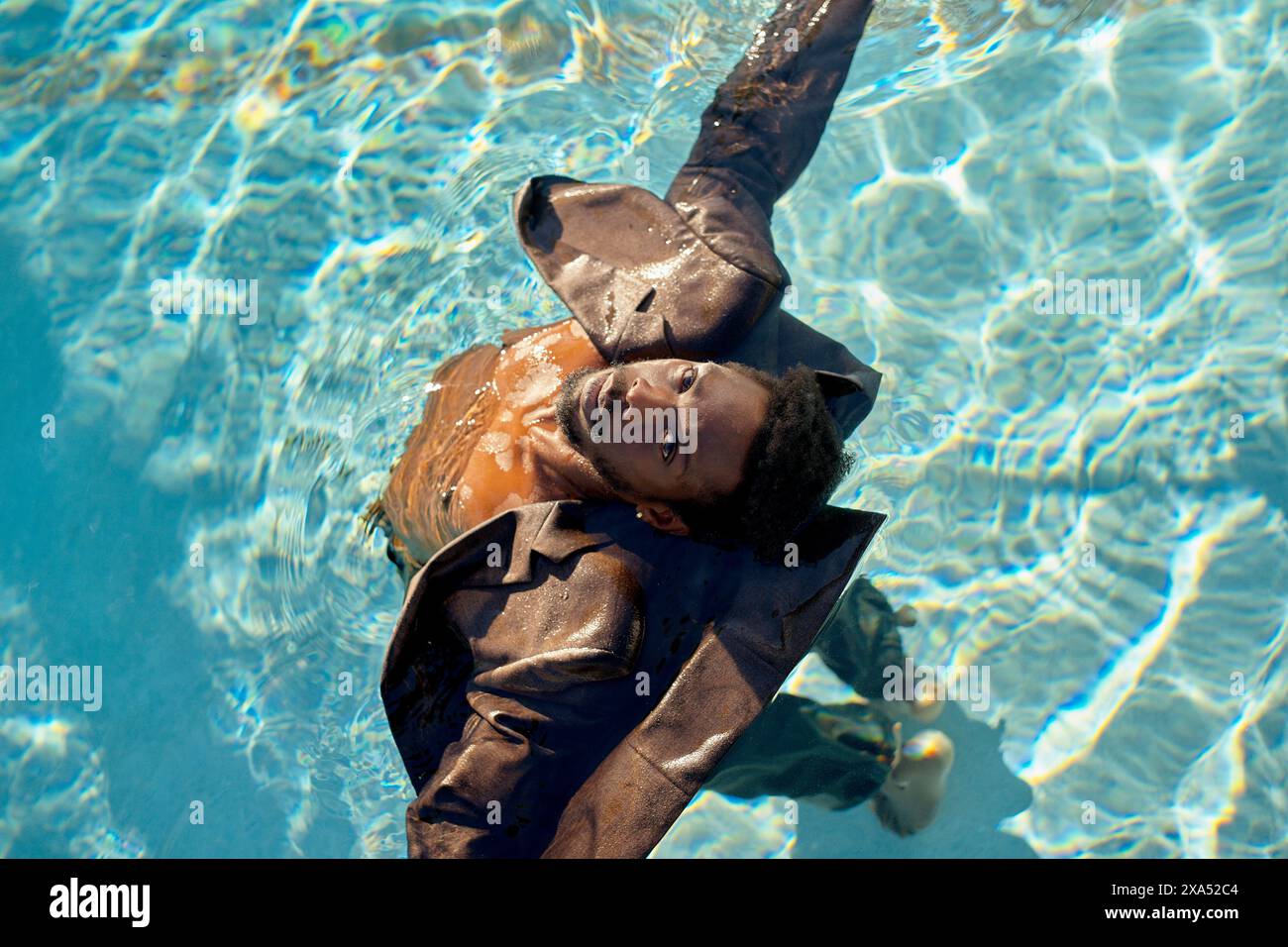 Uomo con una tuta che galleggia serenamente sulla schiena in una piscina azzurra sotto la luce del sole. Foto Stock