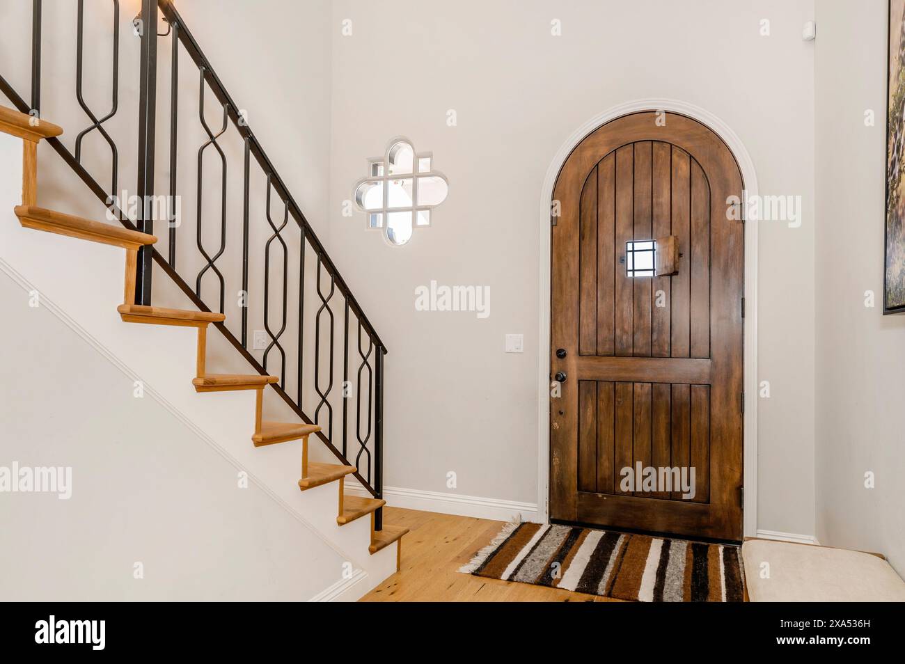 Ingresso dalle pareti bianche con porta in legno e ringhiera in ferro nera Foto Stock