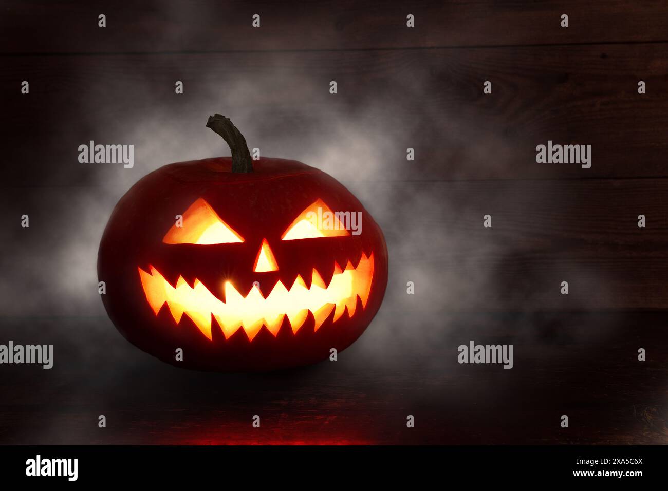 Spaventosa zucca di Halloween con gli occhi che brillano all'interno su sfondo scuro. Spaventosa zucca di Halloween, Jack o Lantern, con un volto malvagio e gli occhi su un legno Foto Stock