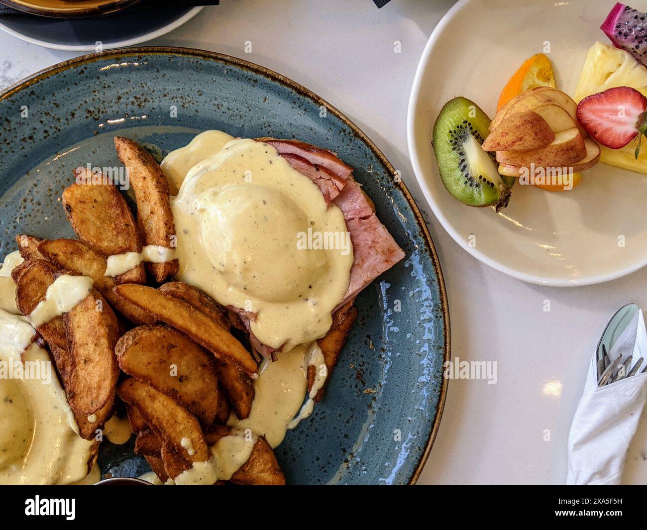 Uova Benedict con prosciutto, patate a spicchi e frutta Foto Stock
