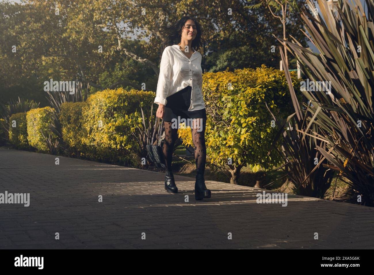 Una donna adulta sta camminando per il parco per lavorare. Indossa calze nere e una camicia bianca Foto Stock