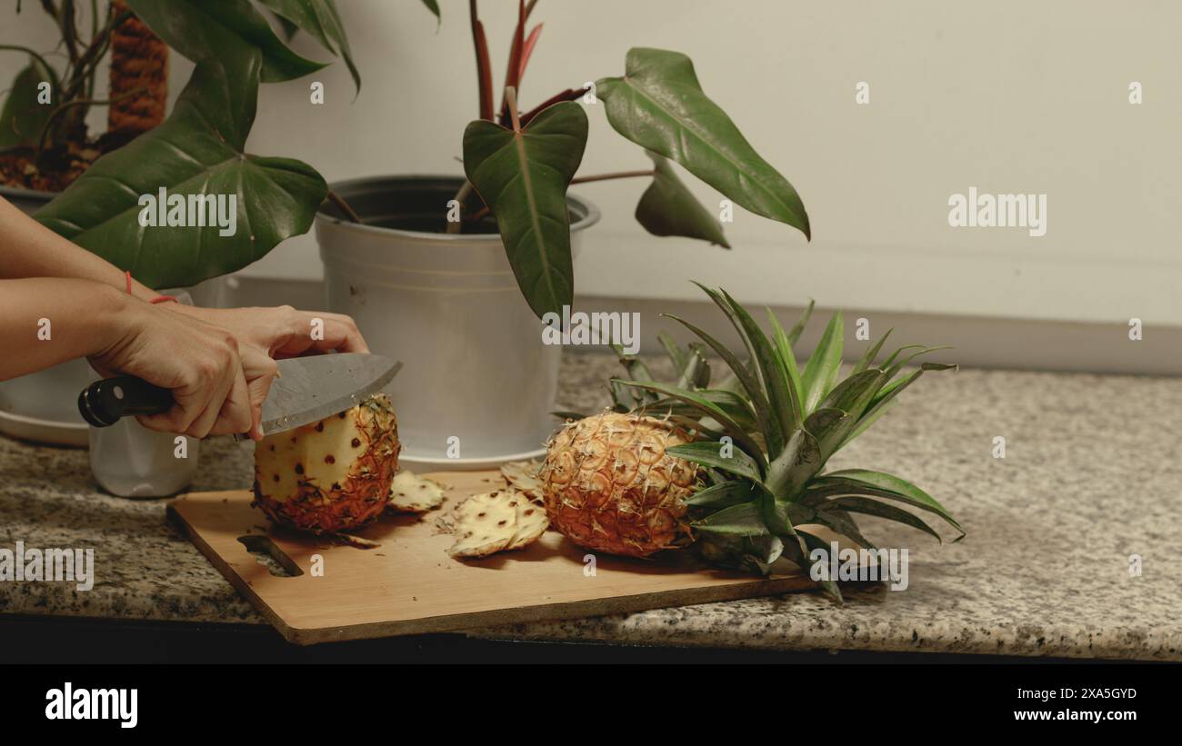 Le mani di una persona sbucciano un frutto di ananas usando un coltello per fare uno spuntino estivo vegano sano Foto Stock
