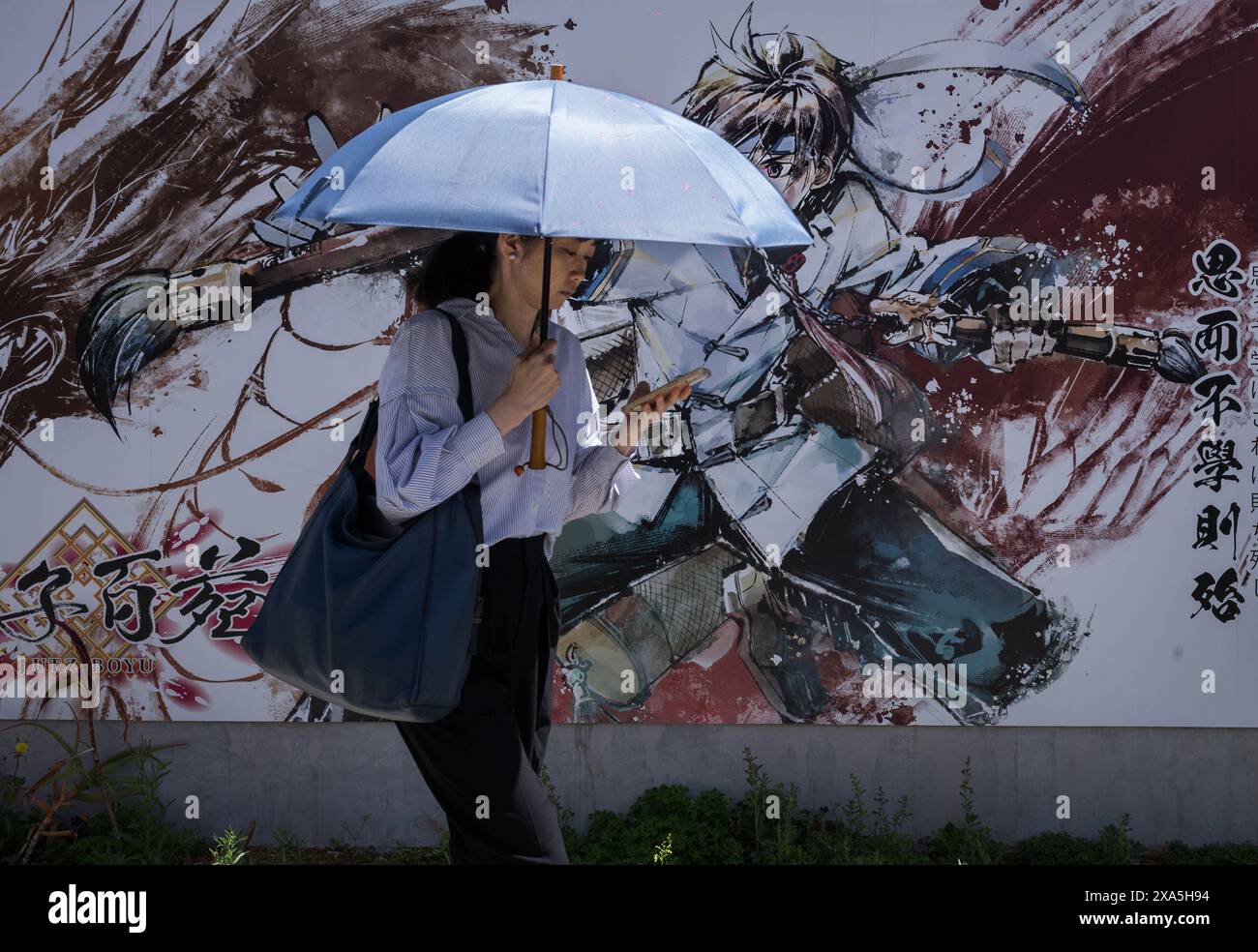 Una donna con un ombrello cammina accanto a un colorato muro di graffiti a Yokohama, in Giappone. Foto Stock