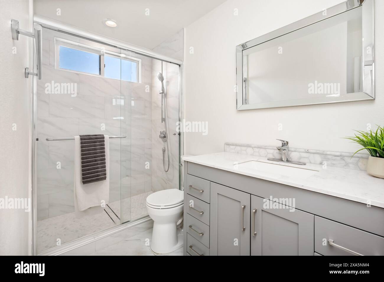 Questa immagine mostra un bagno moderno caratterizzato da una tavolozza di colori neutri. Il bagno è dotato di box doccia in vetro con un asciugamano appeso su una cromata. Foto Stock