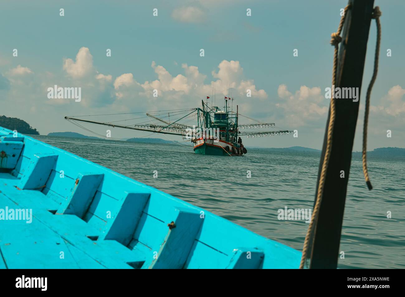 Una barca da pesca viene vista sulle calme acque oceaniche sotto un cielo nuvoloso dalla prua di una barca blu, mostrando un momento sincero della vita quotidiana e del sostentamento in questa zona Foto Stock