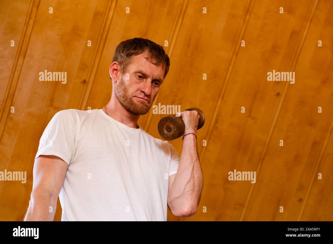 Uomo che solleva pesi in una palestra in legno durante l'allenamento mattutino. Foto Stock
