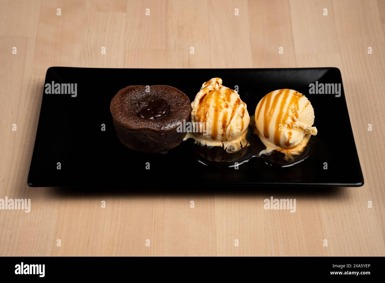 Una deliziosa torta lavica abbinata a una pallina di gelato cremoso su un piatto nero Foto Stock