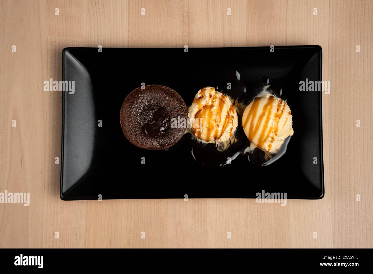 Una deliziosa torta lavica abbinata a una pallina di gelato cremoso su un piatto nero Foto Stock