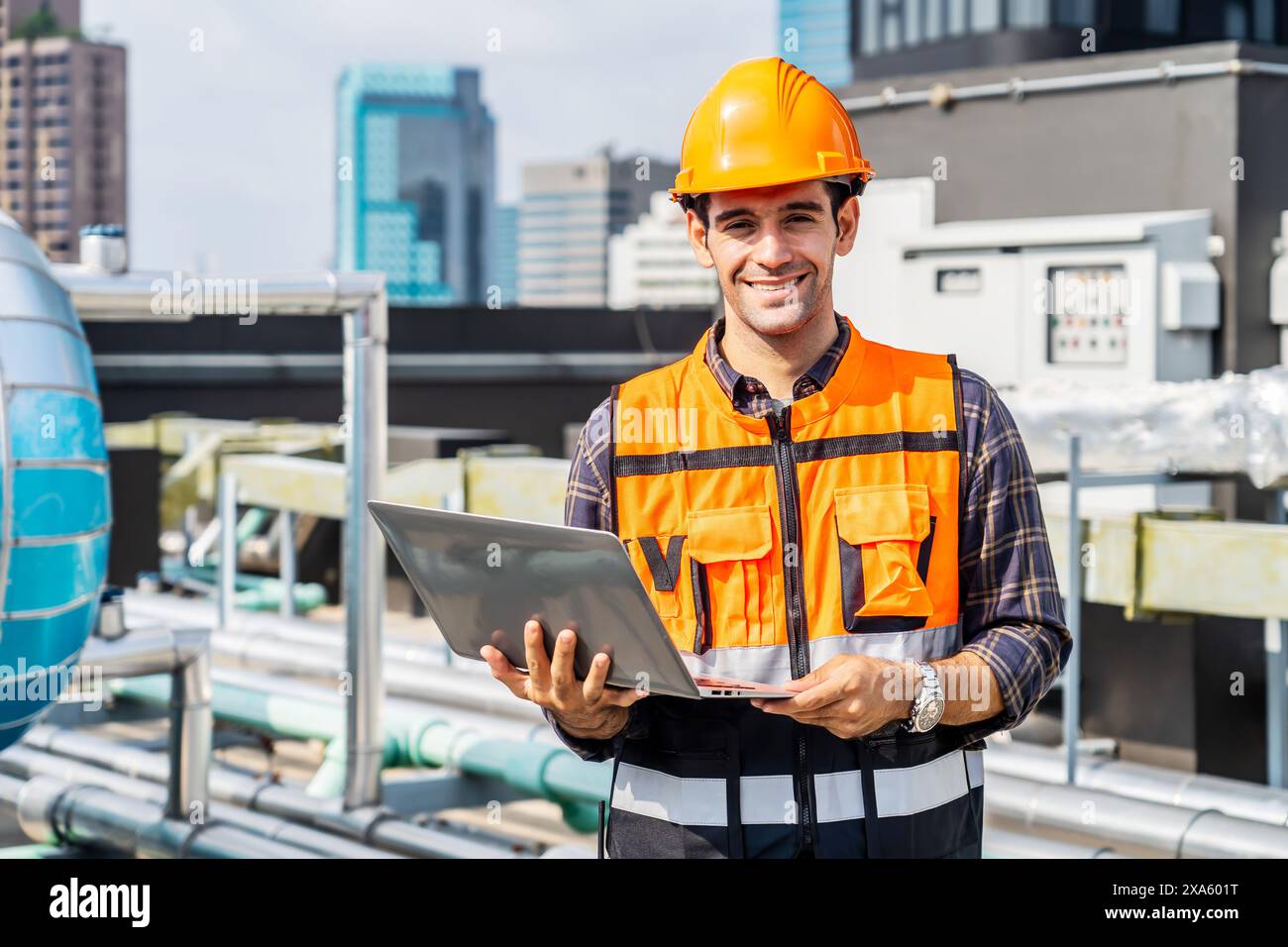Un uomo in elmetto che lavora su un computer portatile vicino a tubi industriali in Thailandia, Bangkok Foto Stock