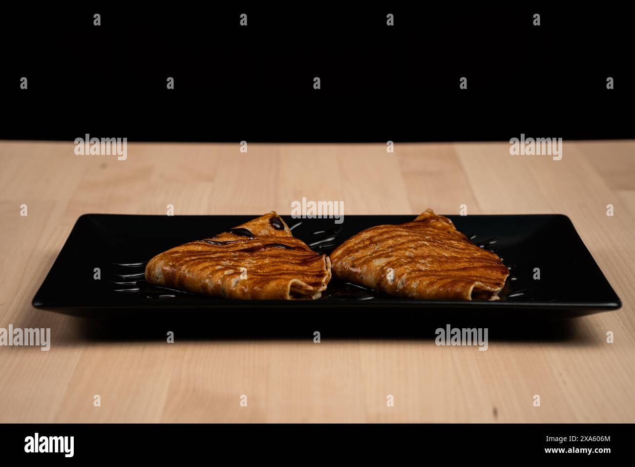 Un piatto di pancake condito con sciroppo su un piatto nero Foto Stock