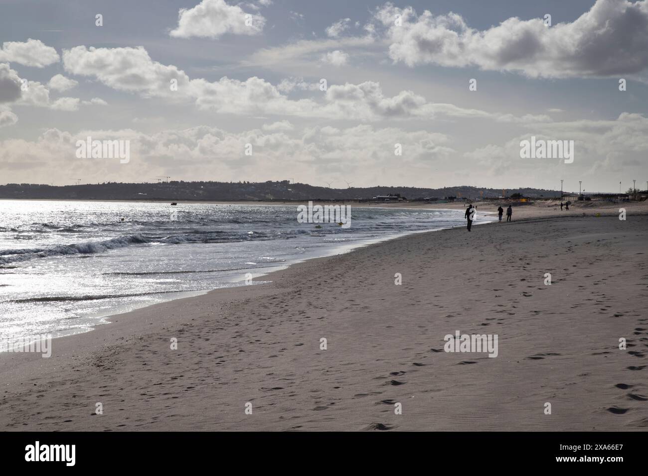 Un gruppo di individui che passeggiano lungo il litorale su una spiaggia sabbiosa Foto Stock