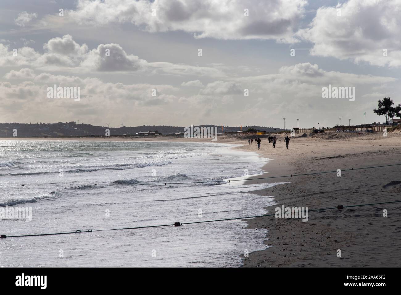 Un gruppo di individui che passeggiano lungo il litorale su una spiaggia sabbiosa Foto Stock