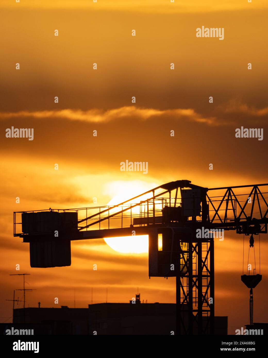 Una silhouette di una gru contro un cielo al tramonto, con un cantiere in primo piano Foto Stock