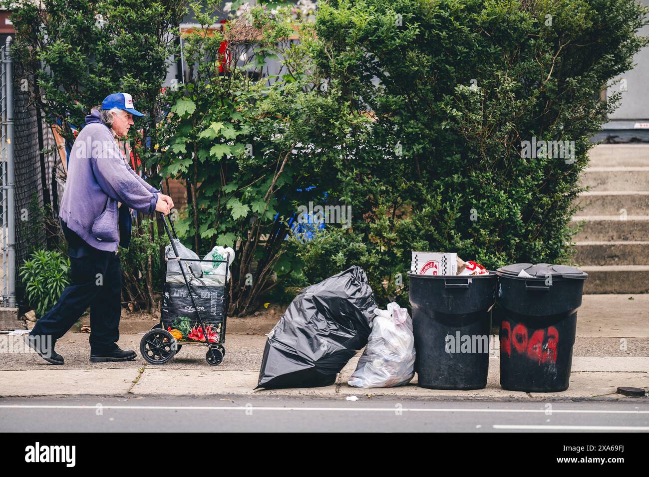 Uomo con sedia a rotelle e borse che passeggiano per strada Foto Stock