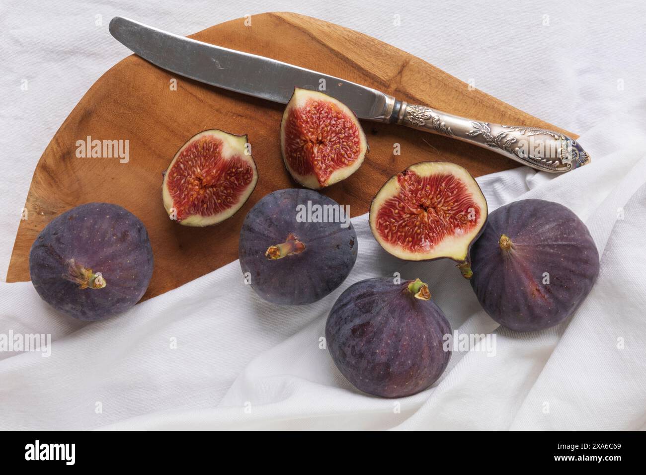 foto da tavolo di un gruppo di frutti di fico tagliati e interi con coltello vintage e tagliere in legno su sfondo tessile bianco Foto Stock