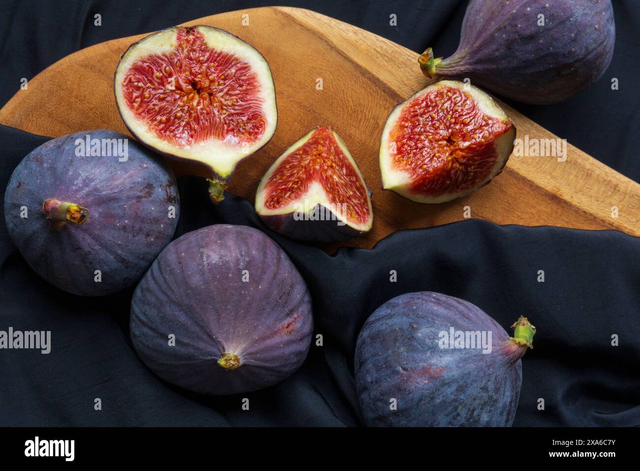 foto ravvicinata di un gruppo di frutti di fico tagliati e interi su un tagliere di legno su sfondo scuro Foto Stock