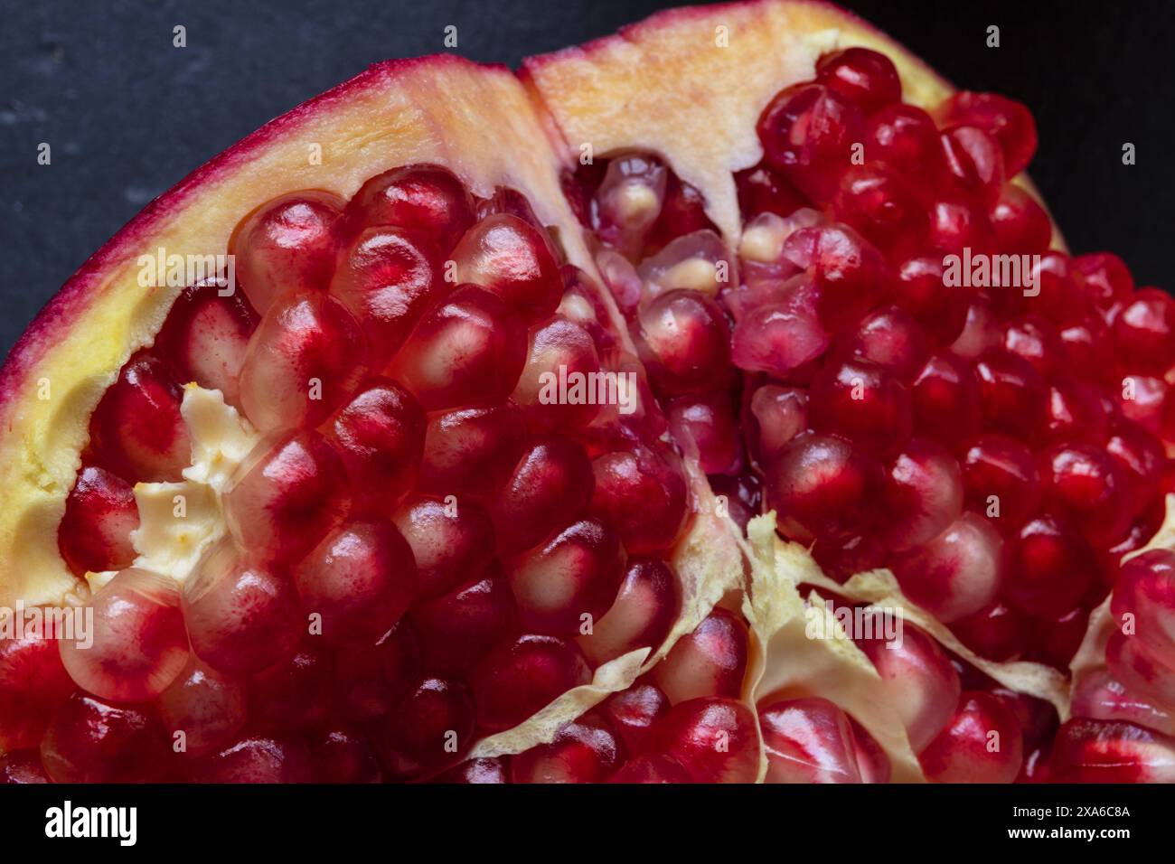 primo piano foto macro di un melograno aperto su sfondo nero scuro, fotografia macro still life con cibo basso Foto Stock