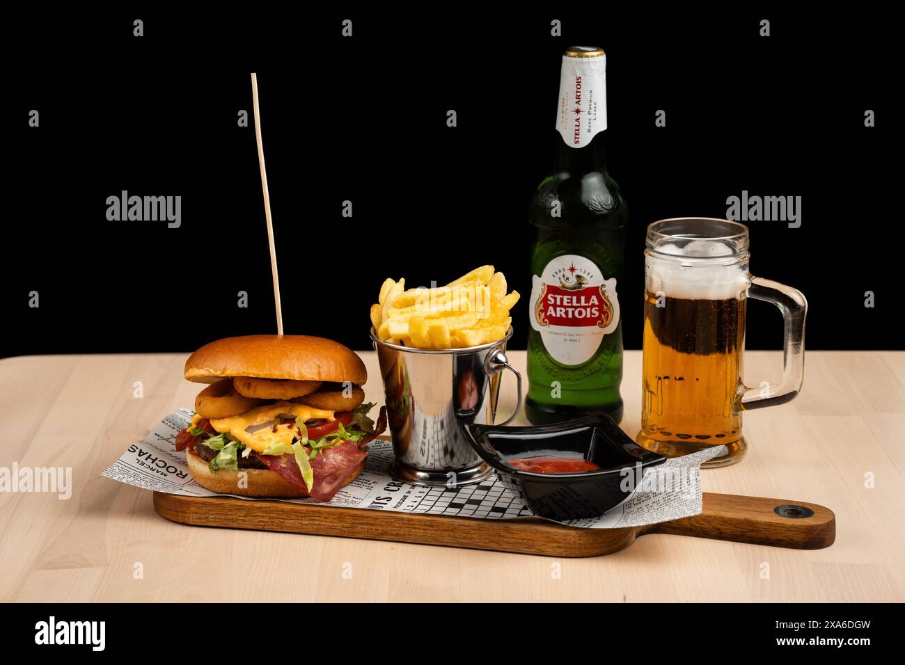 Un vassoio con una bottiglia e un bicchiere di birra Stella Artois, cheeseburger e patatine fritte. Foto Stock