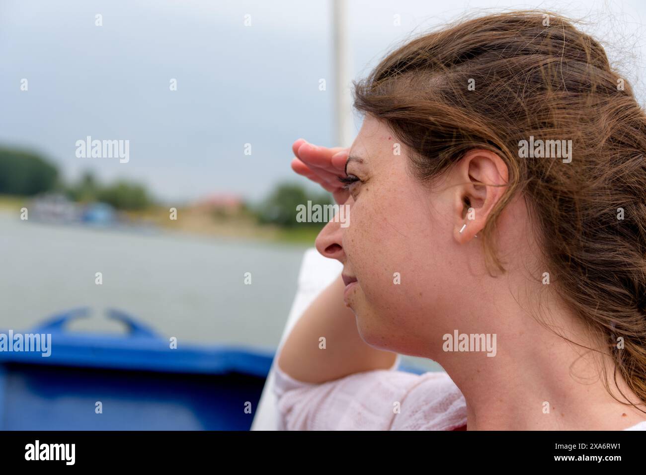 Una donna seduta accanto all'acqua con le mani alzate sugli occhi, che blocca il sole Foto Stock
