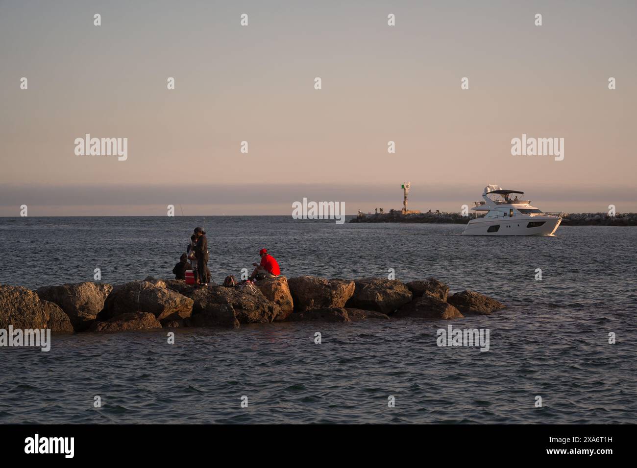 Un gruppo di individui che si trovano sulla costa rocciosa, osservando le barche nel fossato Foto Stock