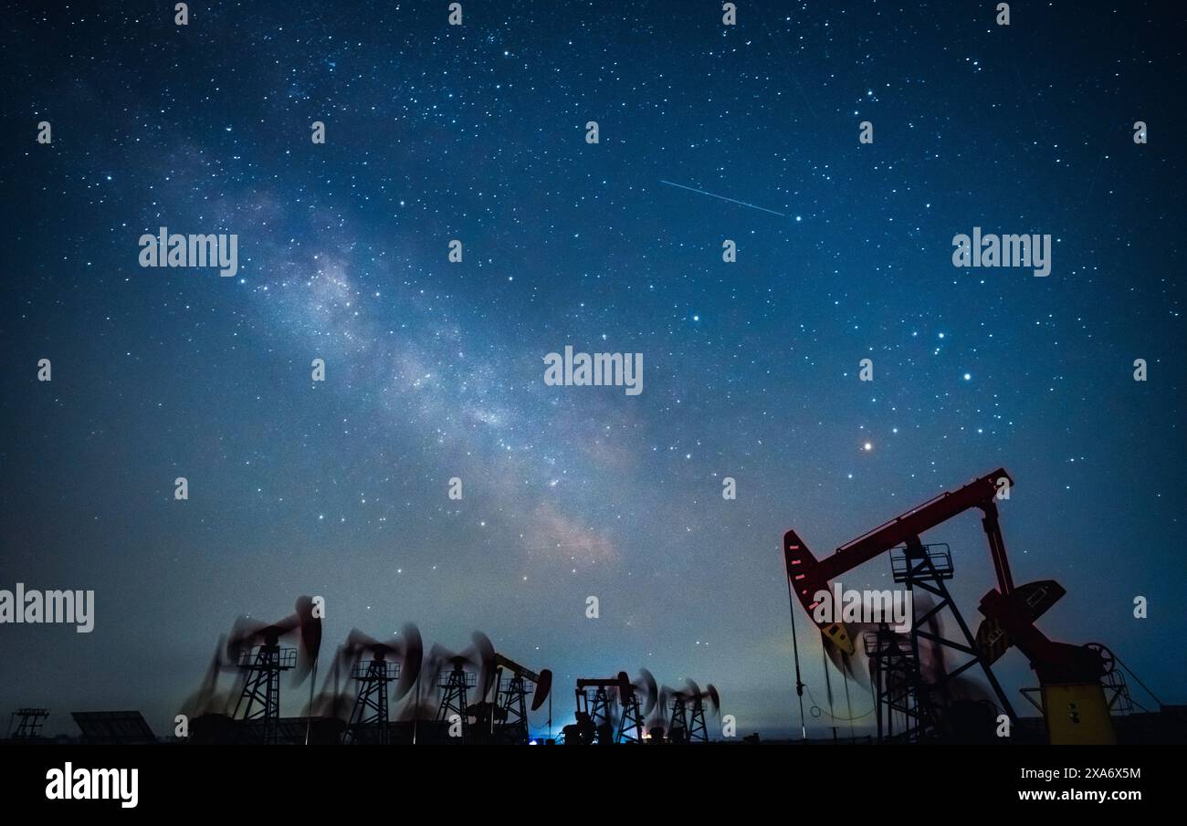 Un gruppo di individui si è riunito vicino alle piattaforme petrolifere sotto il cielo stellato notturno e la via lattea Foto Stock