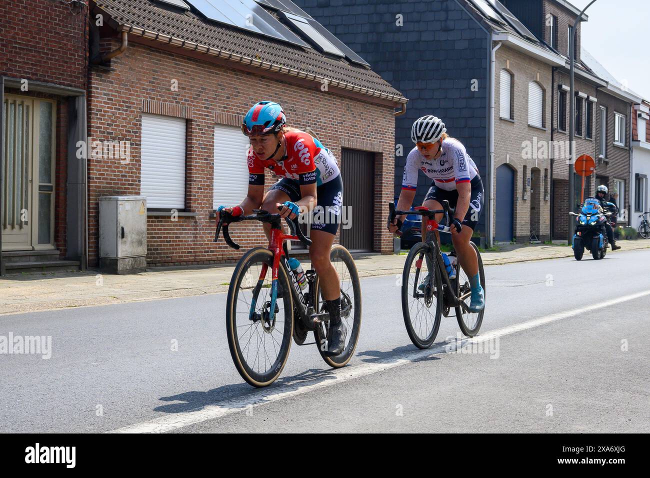 Due ciclisti con casco accanto a case pittoresche su una strada durante la gara ciclistica Foto Stock