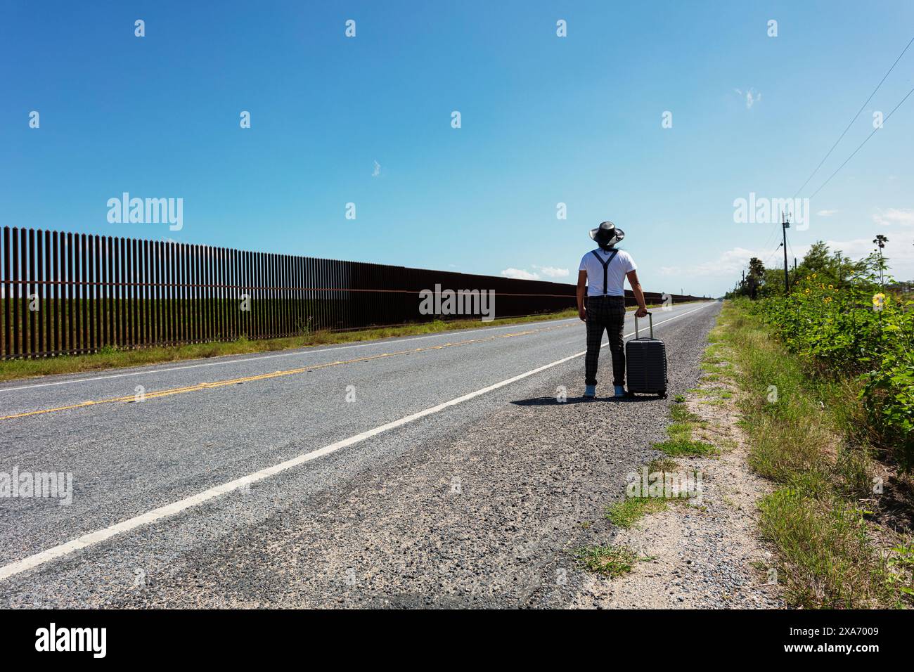 Una persona con una valigia grigia accanto al muro a Brownsville, Texas Foto Stock