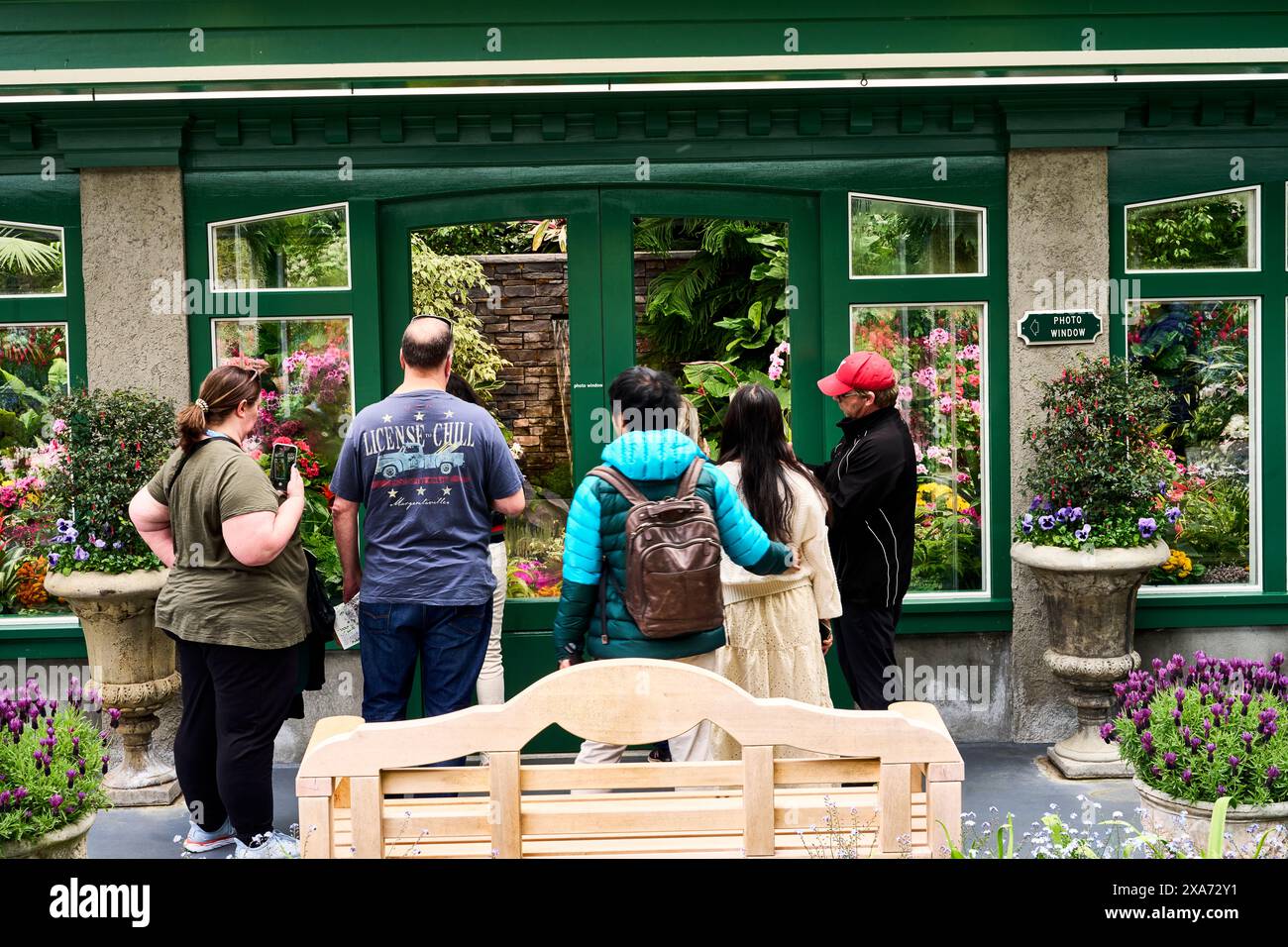 Persone che guardano attraverso la finestra della serra pubblica i fiori splendidamente esposti ai Butchart Gardens, Victoria, British Columbia. Foto Stock