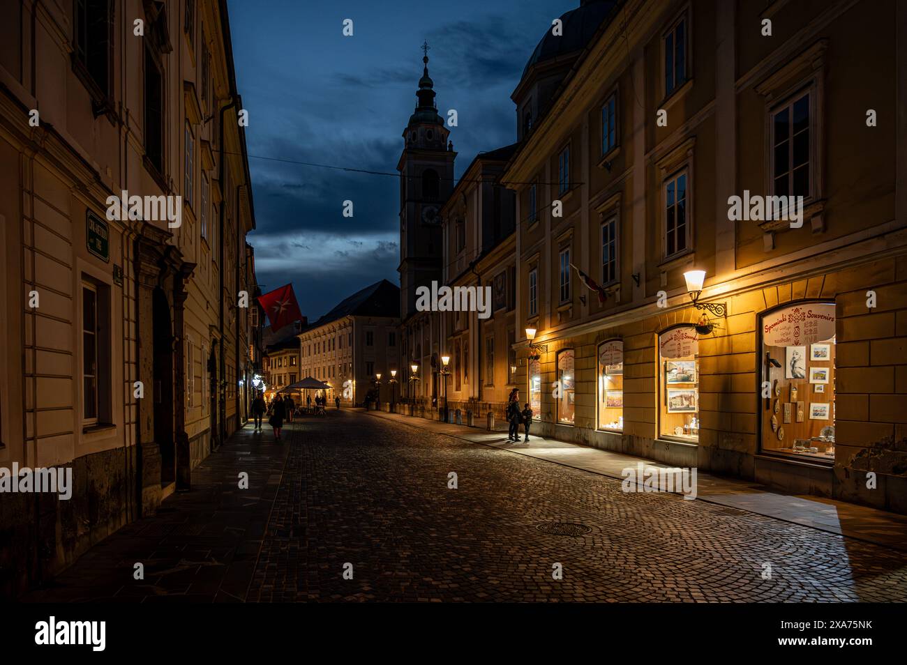 Una storica strada di Lubiana illuminata da luci accese al tramonto Foto Stock