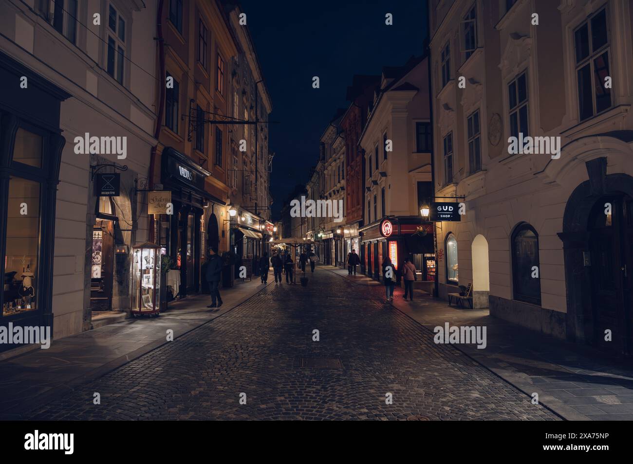 Una scena notturna di una strada illuminata con negozi e gente Foto Stock
