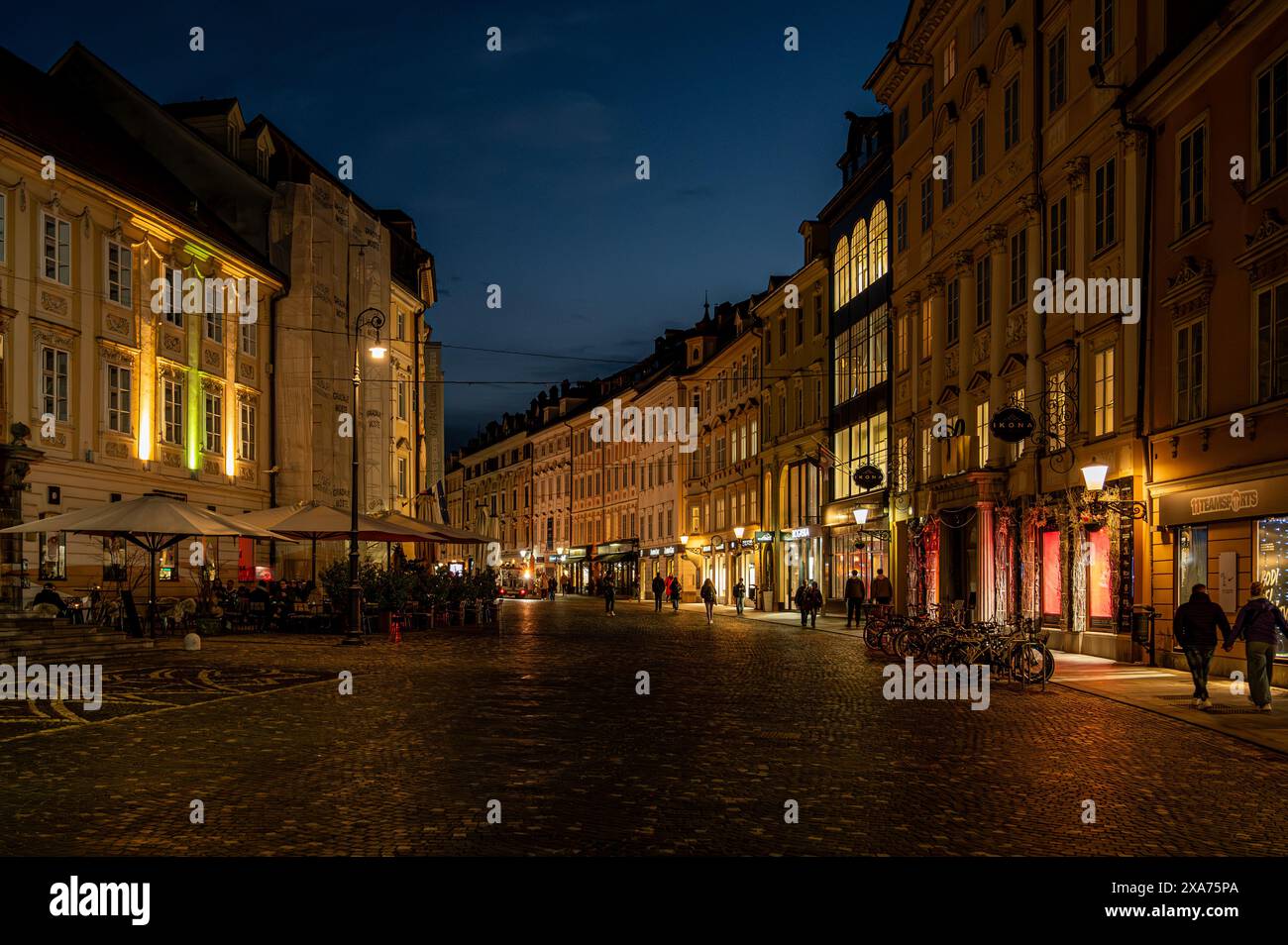 Una storica strada di Lubiana illuminata da luci accese al tramonto Foto Stock