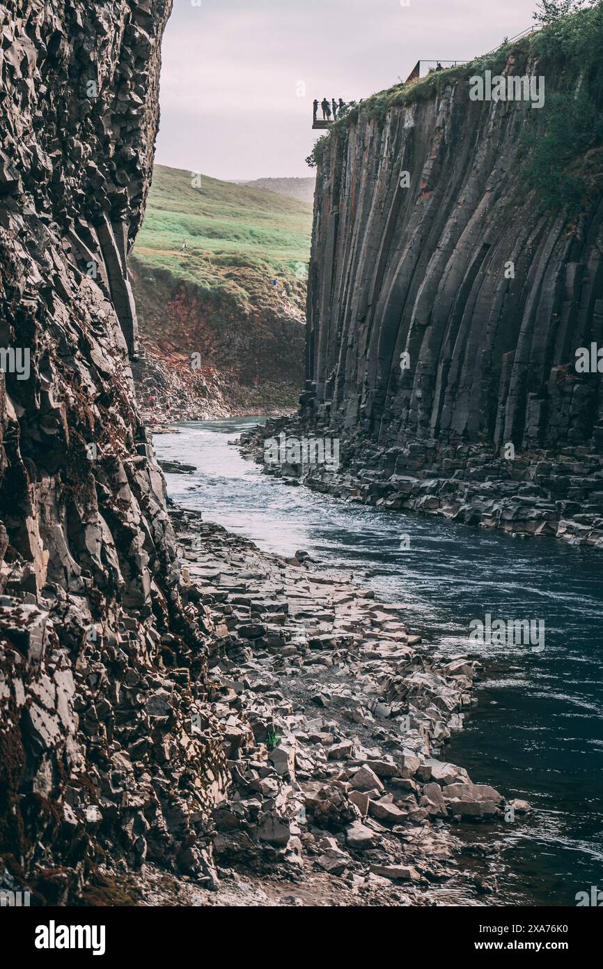 Un gruppo di individui ai piedi di una scogliera torreggiante, che guarda un fiume sottostante a Studlagil, in Islanda Foto Stock