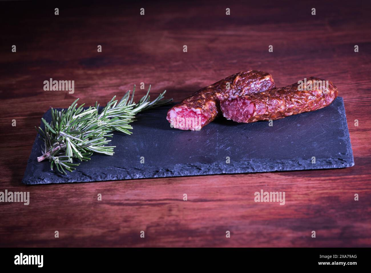 Una dose ravvicinata di salsiccia a fette e ramoscello di pino su una lastra di pietra Foto Stock