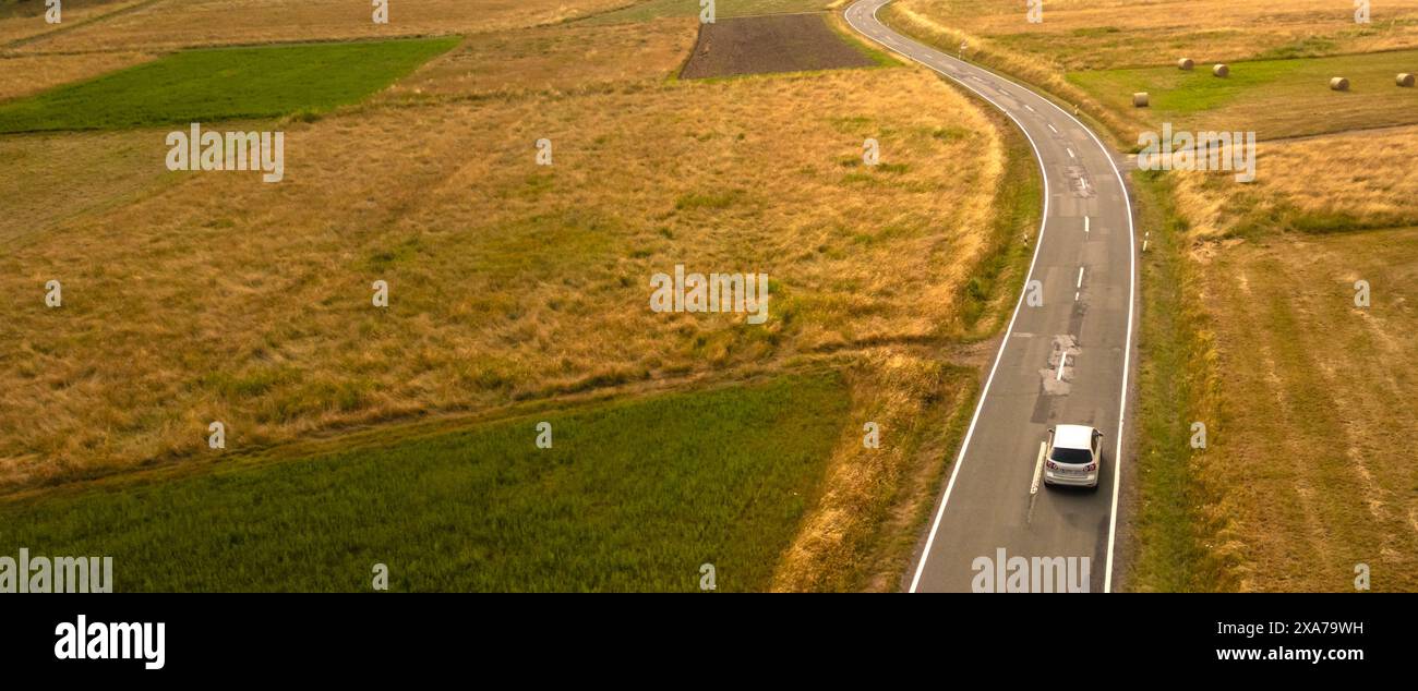 Auto sulla strada tortuosa tra i campi dorati in estate Foto Stock