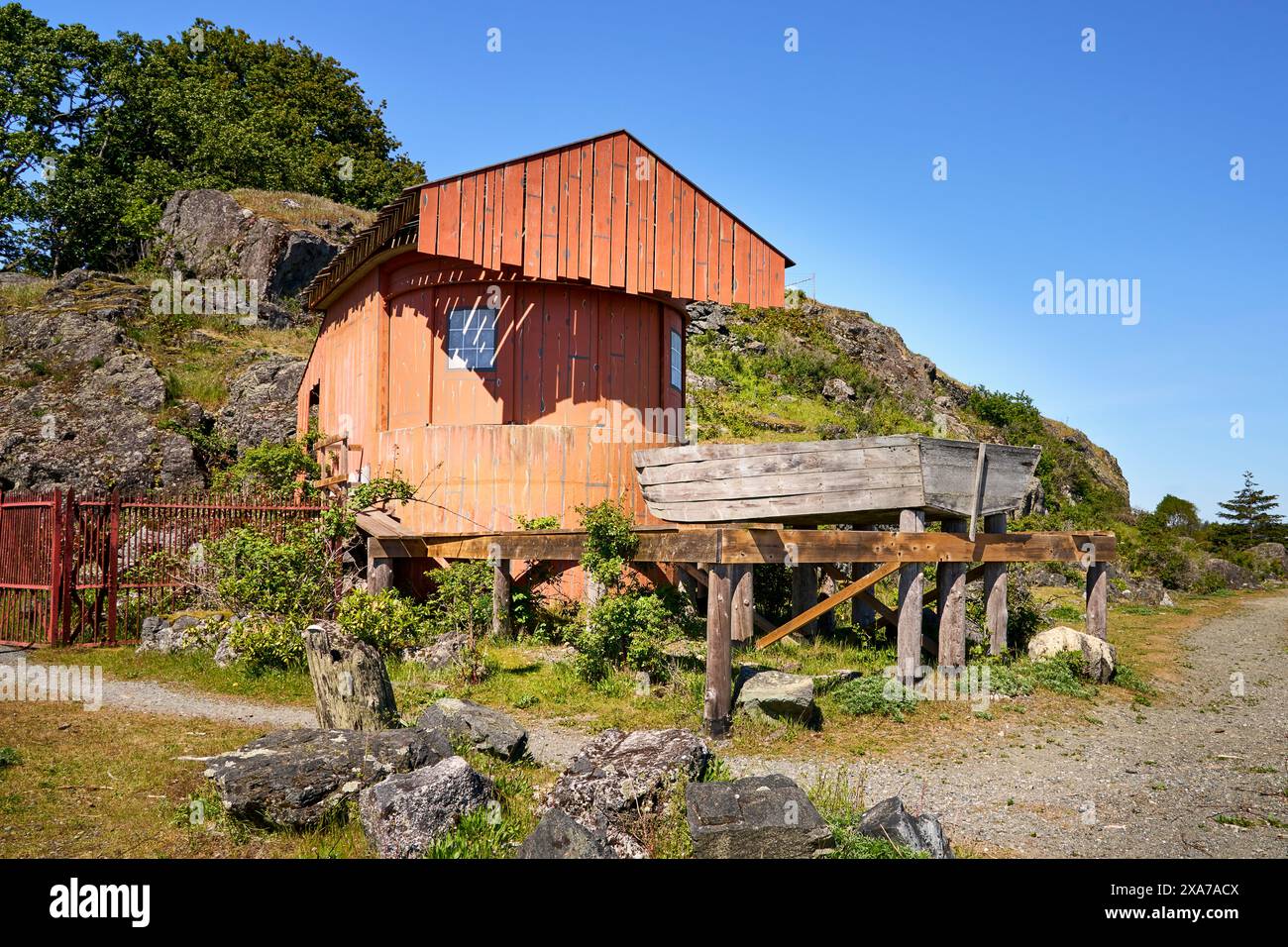 Un rustico capannone di barche dipinte di arancio con uno scavo di legno su una piattaforma rialzata in una destinazione popolare. Foto Stock