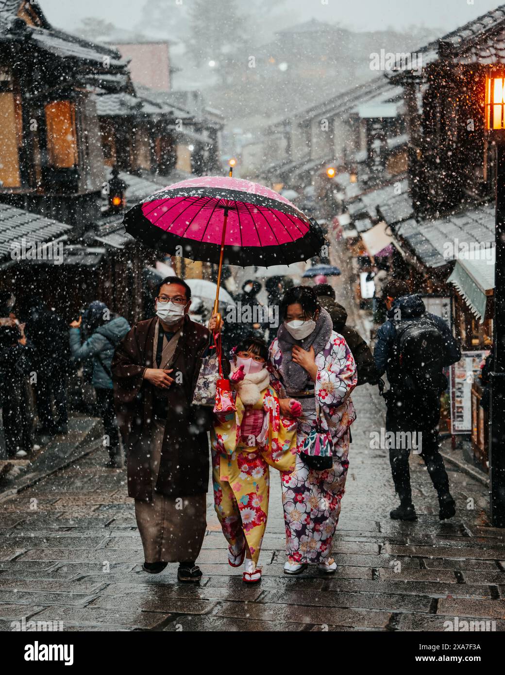 Una famiglia che cammina lungo una strada innevata, condividendo un ombrello Foto Stock