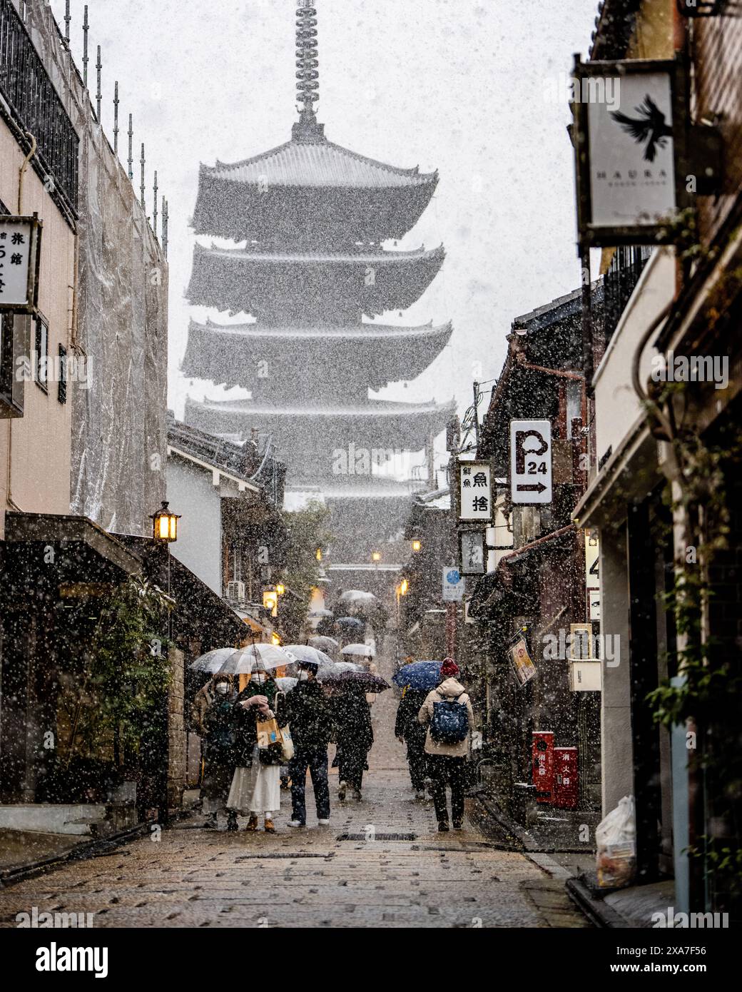 Un gruppo di persone passeggia sulla neve tra edifici d'epoca con ombrelloni Foto Stock