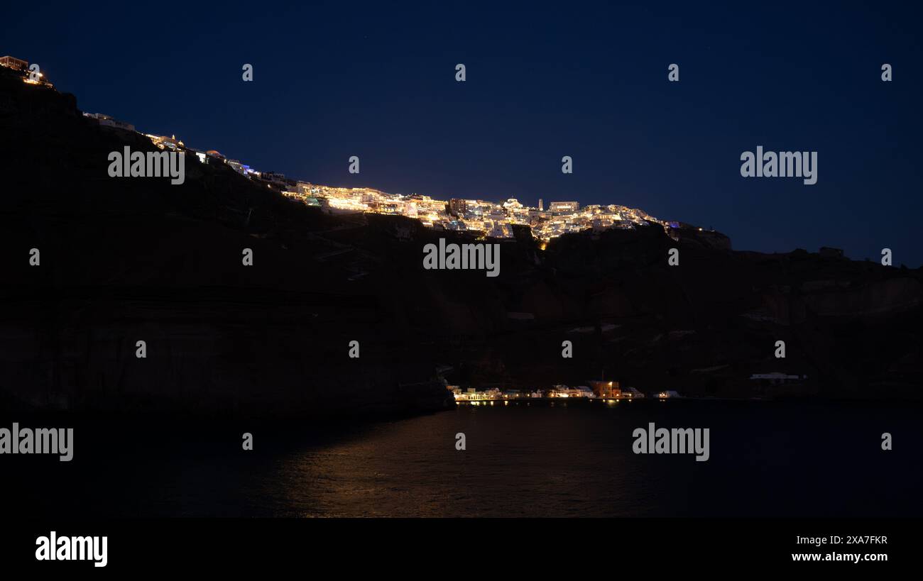 Le luci della città brillano su una collina dall'acqua di notte Foto Stock