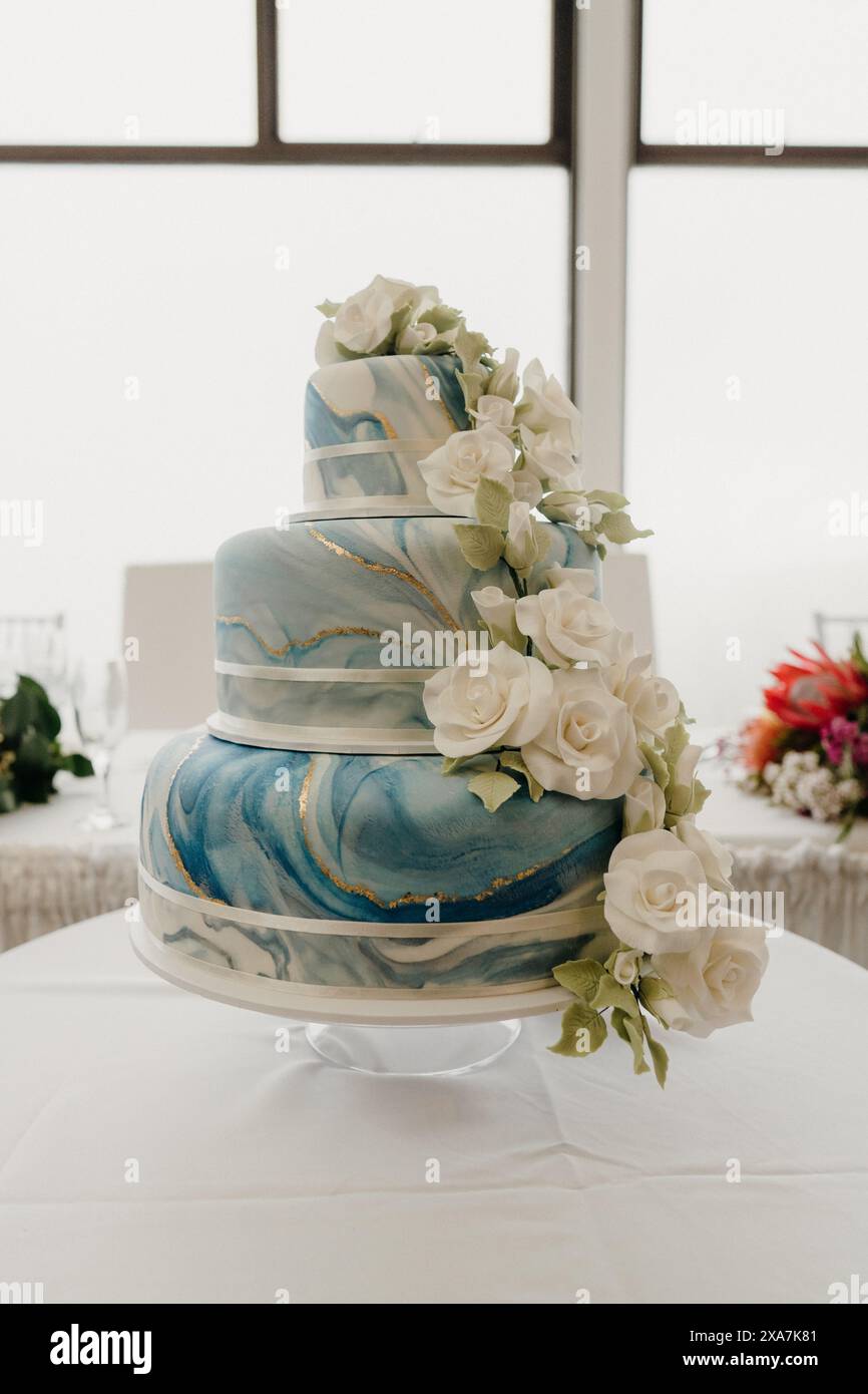 Grande torta nuziale decorata con rose bianche e glassa blu Foto Stock