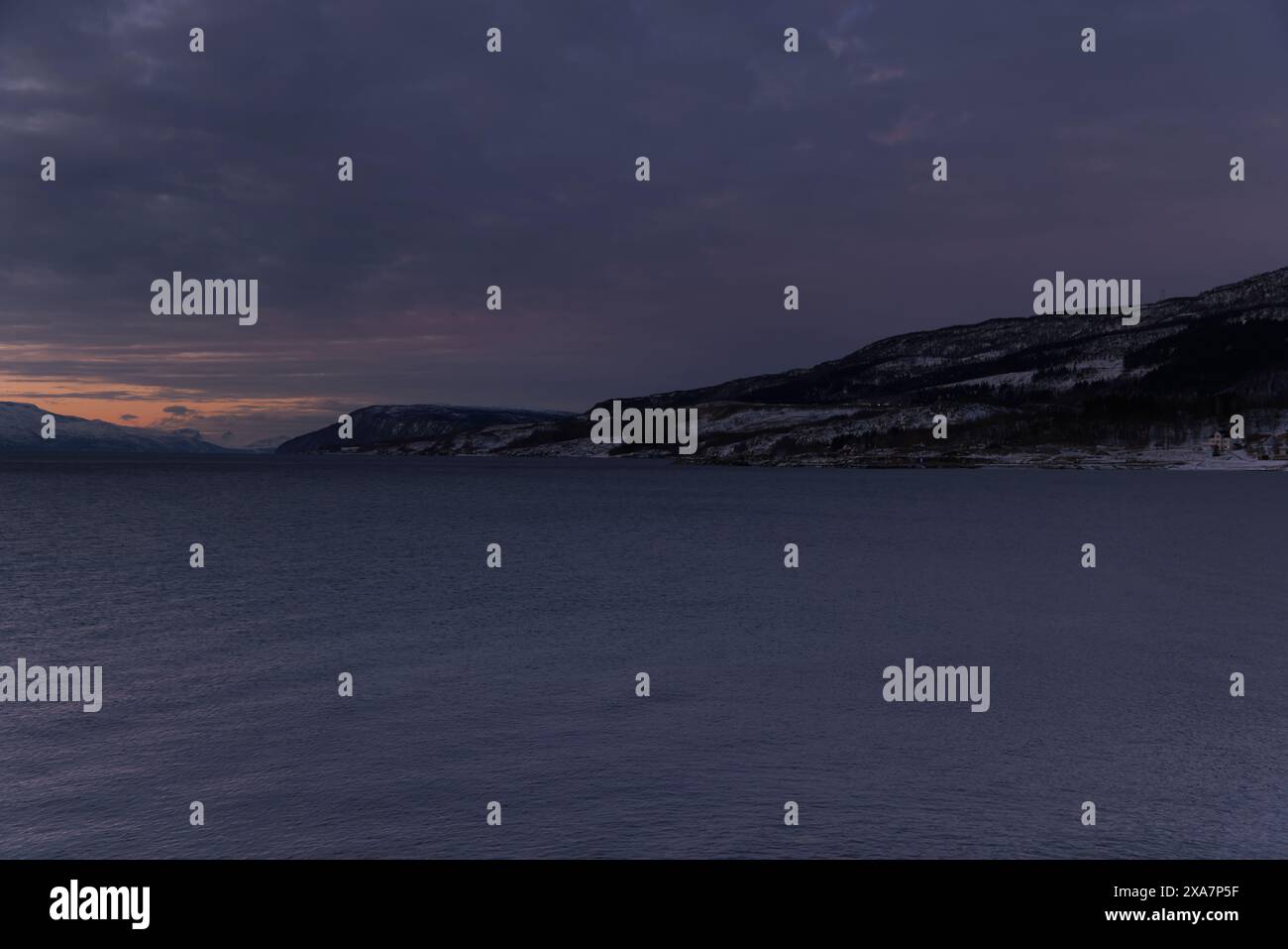 Il sole si stende su un campo innevato con montagne sullo sfondo Foto Stock