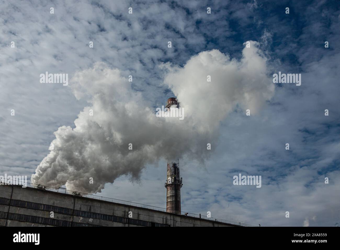 Fumo bianco e grigio e vapore da un alto camino di cemento contro il cielo blu brillante. Foto Stock