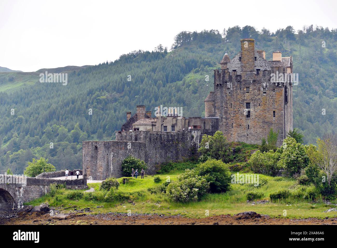 Il castello illuminato di Eilean Donan si riflette nell'acqua in una serata tranquilla, un vecchio ponte di pietra, location cinematografica per James Bond, Highlander e Rob Roy Foto Stock