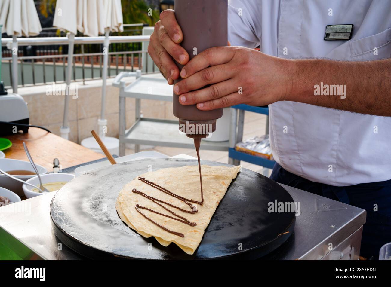 Un uomo sta preparando un dessert con salsa al cioccolato. Il dessert è su un piatto e la salsa viene gocciolata sopra di esso. L'uomo è concentrato sul suo compito e.. Foto Stock