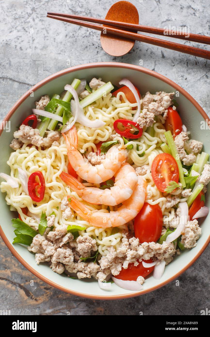 Insalata piccante composta da spaghetti istantanei, gamberi, maiale, verdure e condimento con salsa calda, piatto tipico thailandese sul tavolo di marmo. Verticale Foto Stock