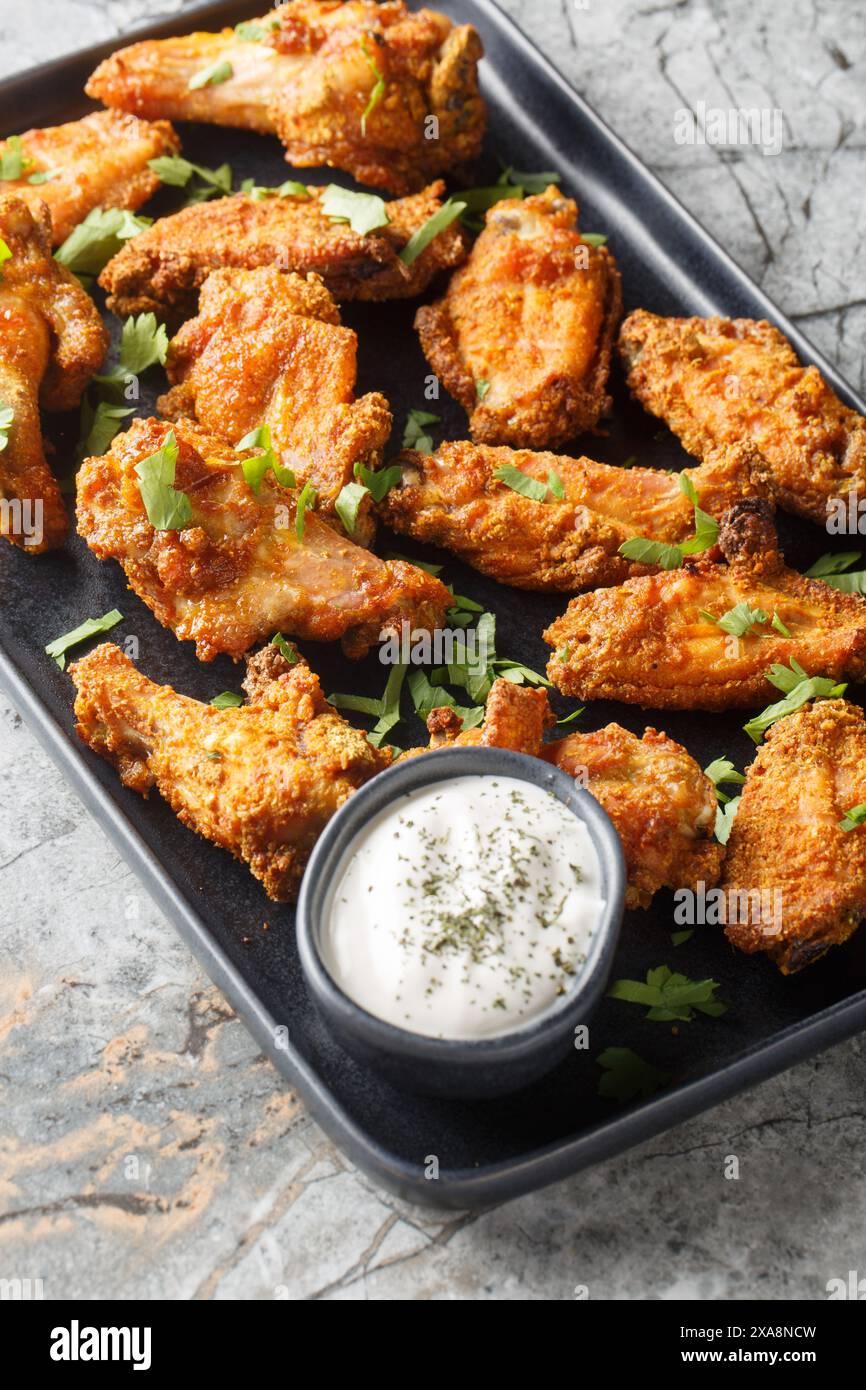 Ali di pollo al curry croccanti serviti con un primo piano di yogurt greco sul piatto del tavolo di marmo. Verticale Foto Stock