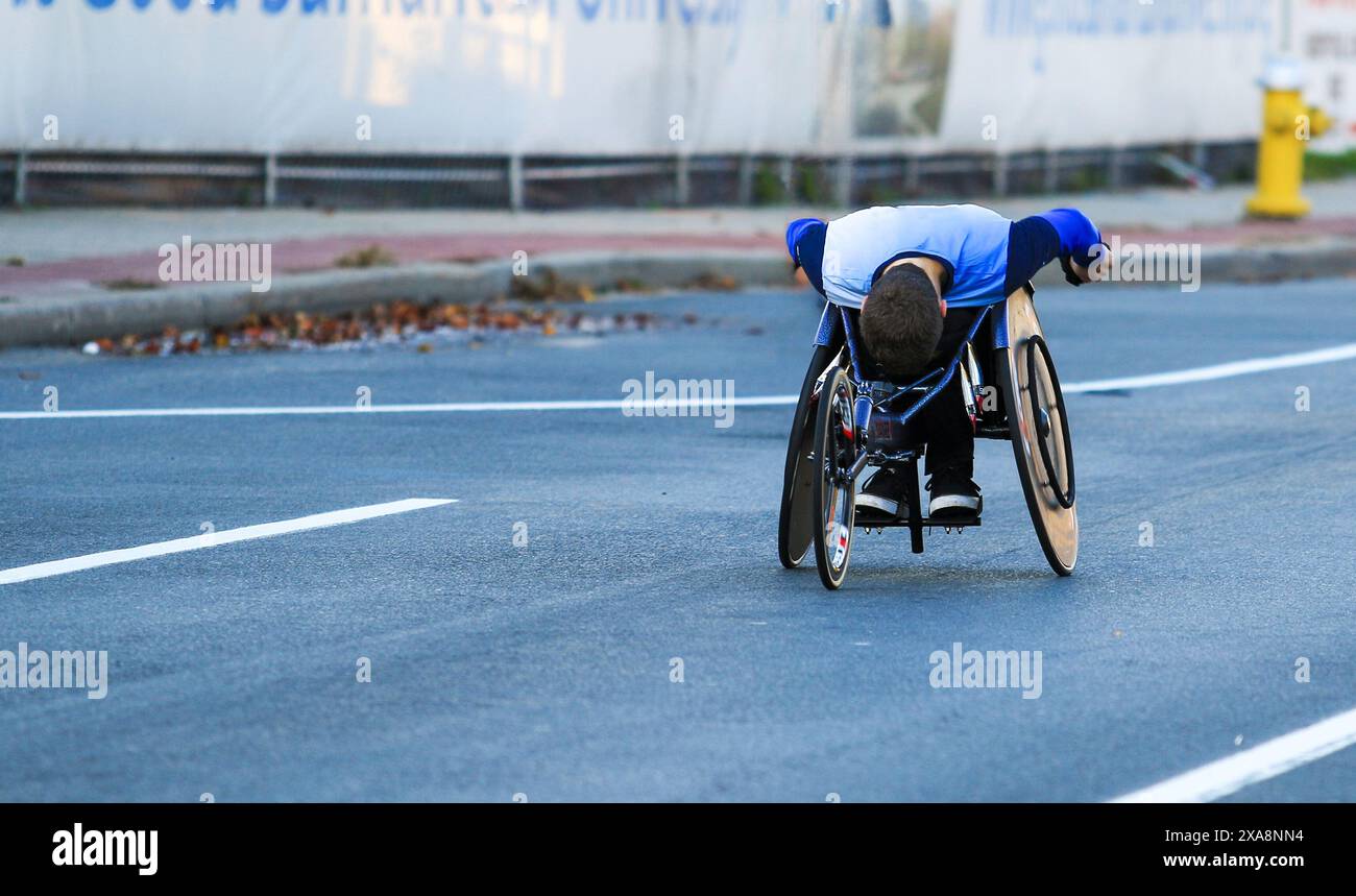 Un giovane su una sedia a rotelle che si muove lungo la strada mentre gareggia in una maratona a Long Island a New York. Foto Stock