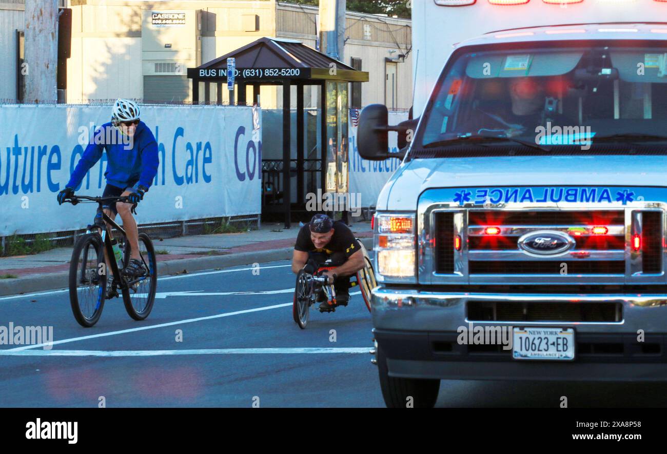 Babylon, New York, Stati Uniti d'America - 22 ottobre 2023: Un atleta in sedia a rotelle che parla per supportare la guida personale di una bicicletta durante una maratona in sella a un'ambu Foto Stock