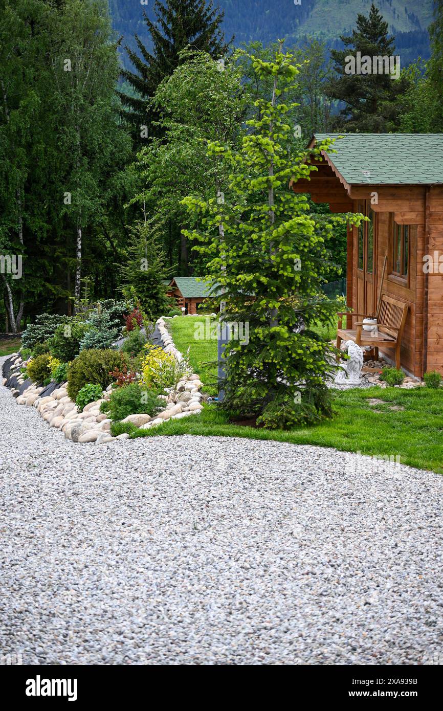 Vista pittoresca di un sentiero del giardino con vegetazione lussureggiante che conduce ad un'accogliente cabina in legno. Foto Stock