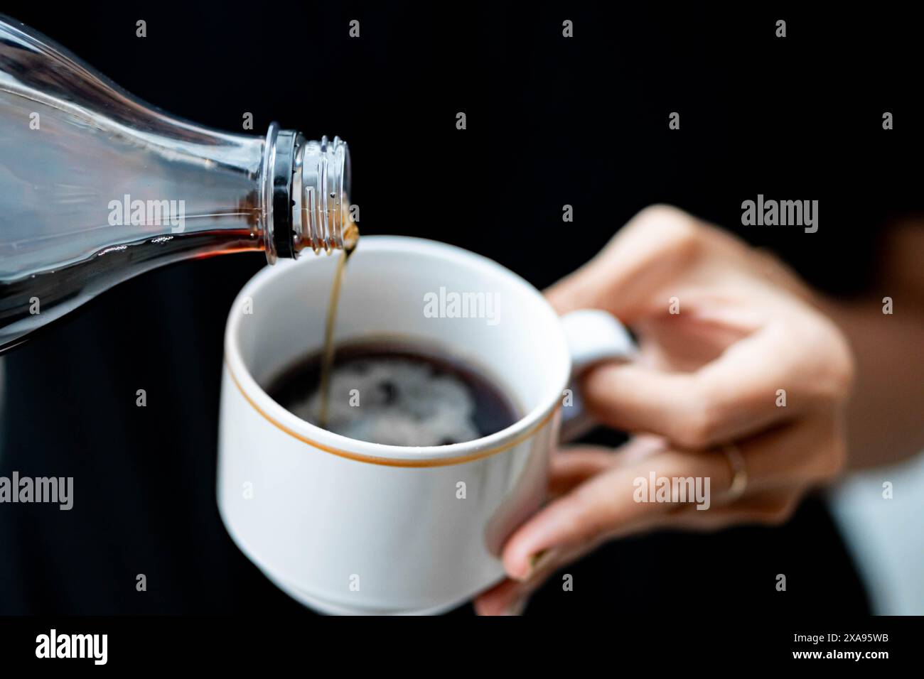 Primo piano di una persona che versa soda in una tazza di caffè bianco. Foto Stock